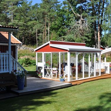 Miljöbild på fristående uterum med funkistak, mellan två stugor.