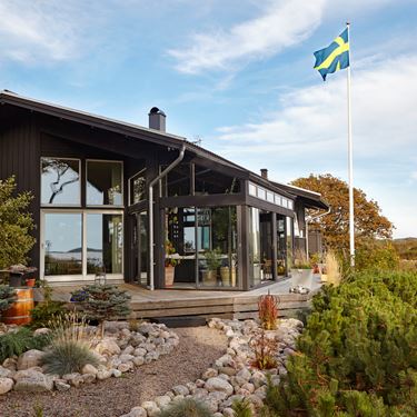 Modernt, svart uterum med generösa glaspartier i lantlig miljö.